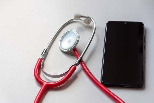 El estetoscopio rojo en el teléfono inteligente negro representa registros médicos y registros digitales de pacientes con dispositivos móviles para médicos digitales y tratamiento de diagnóstico digital con equipos y tecnología modernos - Foto, Imagen