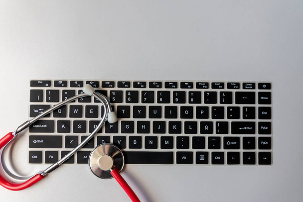 Rotes Stethoskop auf schwarzer Computertastatur auf weißem Schreibtisch zeigt digitale Arztpraxis mit digitalen Patientenakten für medizinische Diagnose und kardiologische Messung mit Antivirus-Checkup-Hackerangriff - Foto, Bild