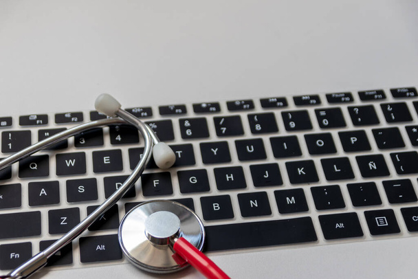 Rotes Stethoskop auf schwarzer Computertastatur auf weißem Schreibtisch zeigt digitale Arztpraxis mit digitalen Patientenakten für medizinische Diagnose und kardiologische Messung mit Antivirus-Checkup-Hackerangriff - Foto, Bild