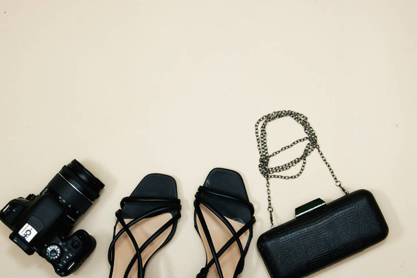 par de sandalias de tacón femenino negro y bolso o embrague con cámara sobre fondo rosa - Foto, imagen