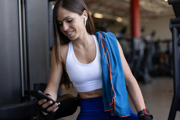 junge Sportlerin schaut in der Turnhalle auf ihr Handy - Foto, Bild