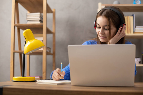 Tyttö puhuu kuulokkeilla ja kirjoittaa muistikirjassa. Opiskelija nainen verkossa larning. Luova inspiraatio tutkimuksen käsite - Valokuva, kuva