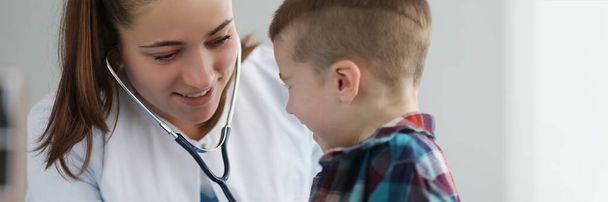 Portret młodej pediatry słucha dziecka z narzędziem stetoskopowym na planowanej kontroli. Spotkanie w klinice w celu zbadania stanu zdrowia. Koncepcja zdrowia - Zdjęcie, obraz