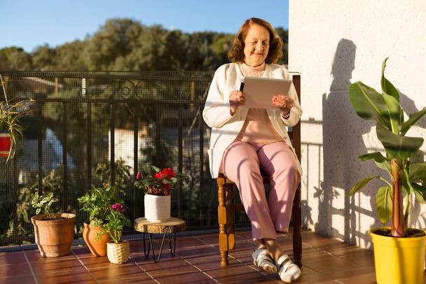 Літня кавказька жінка користується цифровим пристроєм на терасі свого будинку. Концепція технології, зв'язку та громадян похилого віку. Простір для тексту. - Фото, зображення