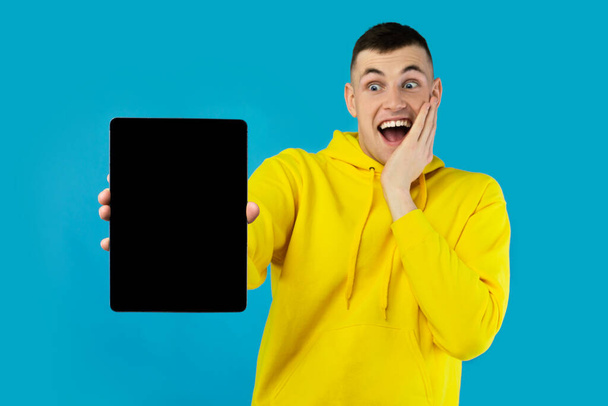 Happy Guy Näytetään digitaalinen tabletti tietokone tyhjä näyttö mainonta verkkosivuilla tai wow tarjous pysyvän poseeraa yli Blue Studio tausta, huutaa jännitystä. Matkijat - Valokuva, kuva