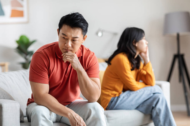 Triste uomo asiatico che litiga con il suo amante, marito coreano premuroso e moglie che hanno una crisi di relazione, seduto sul divano, pensando al divorzio o alla terapia familiare, all'interno della casa - Foto, immagini