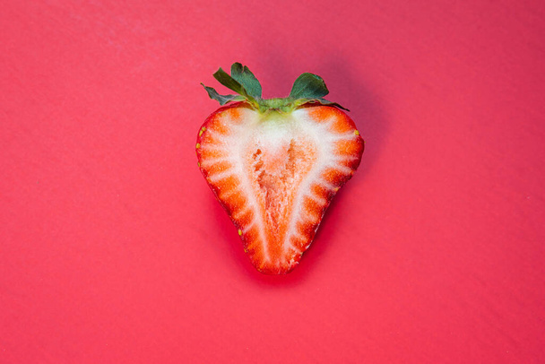 Single sliced ripe red strawberry isolated on a red background - Foto, Bild