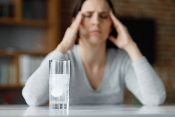 Upset young woman suffering from headache using soluble drug for pain relief. Exhausted woman having painful sensations. Migraine, high blood pressure, chronic fatigue and eyestrain concept. - Foto, afbeelding