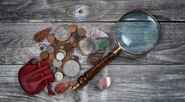 Коллекция редких монет и наконечников стрел коренных американцев с антикварным увеличительным стеклом на деревенском фоне  - Фото, изображение