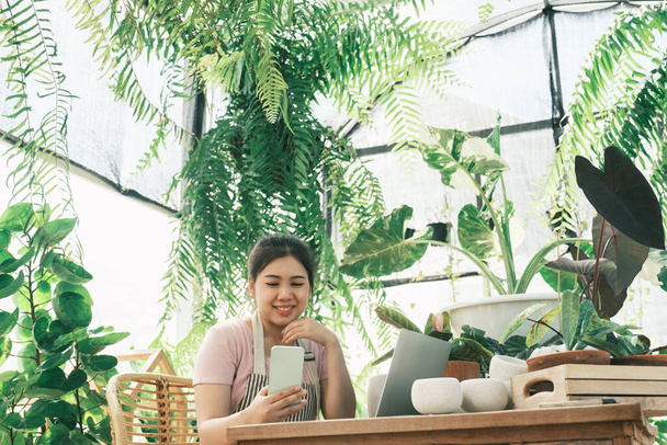Professional florist in florist who provides customer support by phone. young woman writes customer orders during a conversation about cellular work in a greenhouse. - 写真・画像