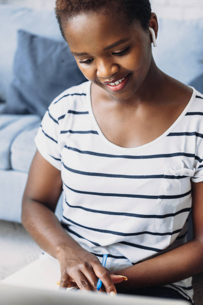 Umfassender afroamerikanischer Student, der Ideen in Tagebuch schreibt, während er zu Hause auf dem Fußboden Hausaufgaben macht. Lernwebinar anschauen. Forschungsarbeit schreiben. - Foto, Bild
