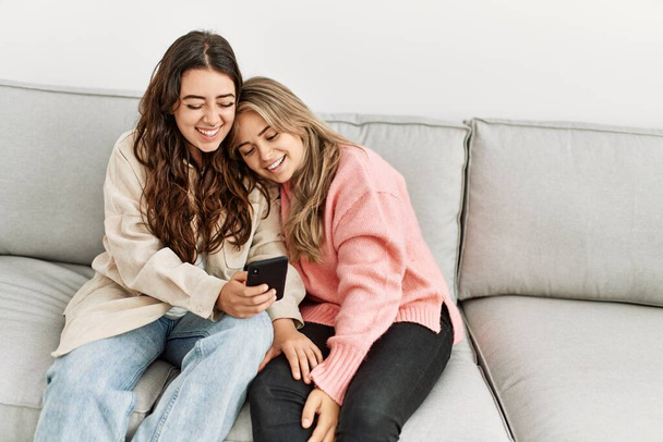Jeune couple souriant heureux en utilisant smartphone assis sur le canapé à la maison. - Photo, image