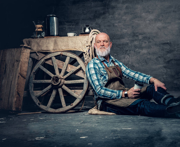 Πορτρέτο του παλαιού barista κάθεται στο πάτωμα γύρω από ντεμοντέ κινητό καφέ του. - Φωτογραφία, εικόνα