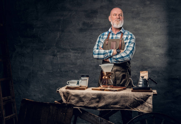 Studio shot of vintage style old man barman with mobile coffee shop against dark background. - Photo, Image