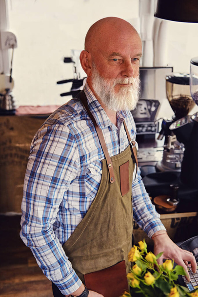 Shot of old barista with long beard and apron in coffee shop with modern equipment. - Photo, Image