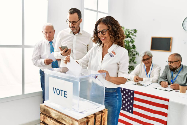 Orta yaşlı Amerikalı seçmen kadın mutlu bir şekilde gülümsüyor oy sandığına koyuyor.. - Fotoğraf, Görsel