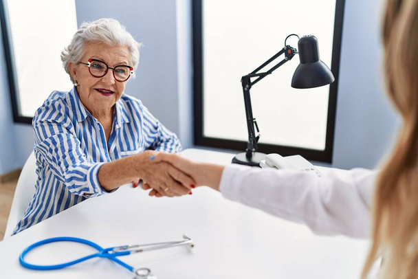 Paciente mayor de cabello gris que recibe consulta médica se da la mano en la clínica - Foto, Imagen