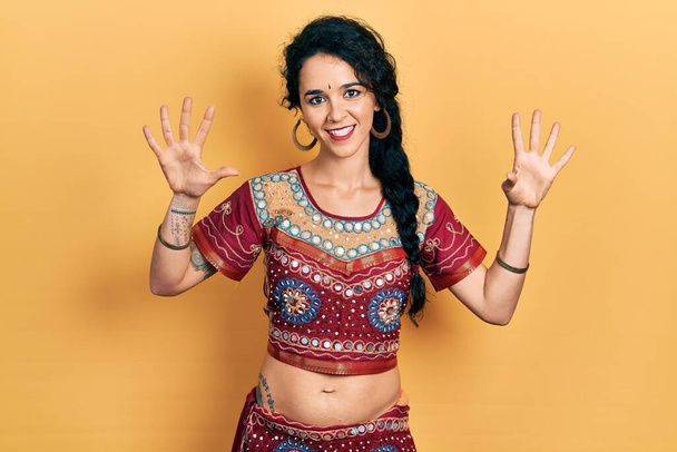 Молодая женщина в бинди и болливудской одежде показывает и показывает пальцами номер девять, улыбаясь уверенно и счастливо.  - Фото, изображение