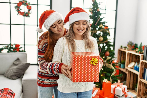vrouw paar knuffelen elkaar houden geschenk stand door kerstboom thuis - Foto, afbeelding