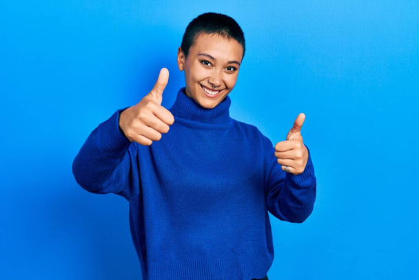 Beautiful hispanic woman with short hair wearing turtleneck sweater approving doing positive gesture with hand, thumbs up smiling and happy for success. winner gesture.  - Fotografie, Obrázek