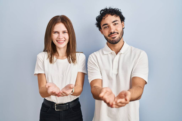 Young couple wearing casual clothes standing together smiling with hands palms together receiving or giving gesture. hold and protection  - Foto, immagini
