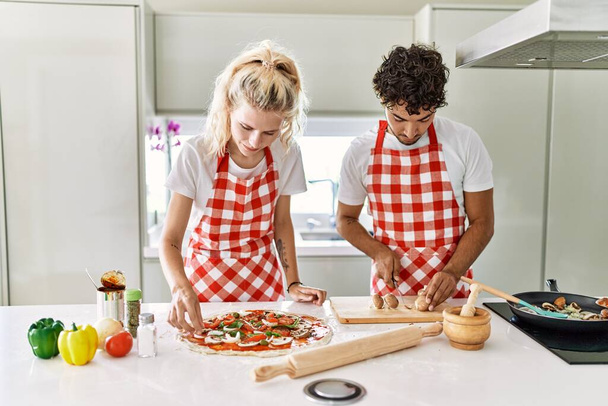 Casal jovem sorrindo feliz cozinhar pizza italiana na cozinha. - Foto, Imagem