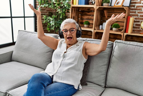 Senior harmaa tukka nainen kuuntelee musiikkia istuu sohvalla kotona - Valokuva, kuva