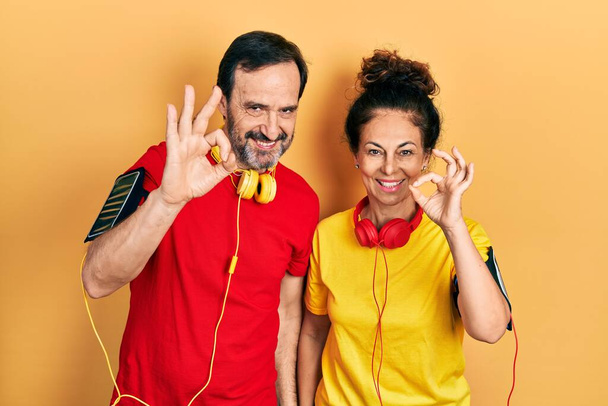 Ein Paar mittleren Alters, hispanische Frauen und Männer in Sportbekleidung und Armreif, die positiv lächeln und mit Händen und Fingern Zeichen setzen. Erfolgreicher Ausdruck.  - Foto, Bild