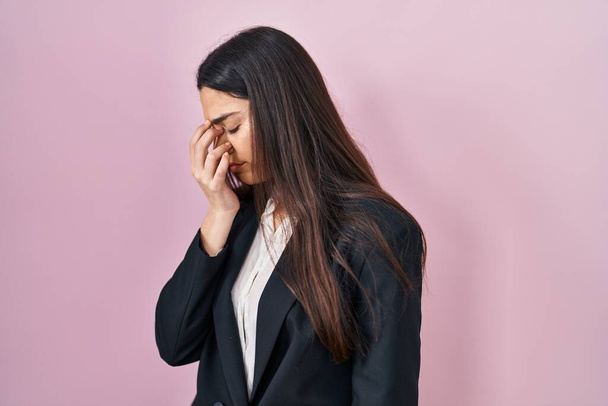 ピンクを背景にビジネススタイルを身に着けている若いブルネットの女性は疲れ鼻をこすり、目は疲労と頭痛を感じている。ストレスとフラストレーションの概念.  - 写真・画像