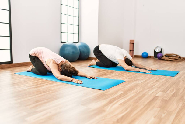 Volwassen Latijns-Amerikaanse echtpaar doen oefeningen en stretching in yoga kamer. Twee volwassen mensen doen pilates en flexibiliteit workout - Foto, afbeelding