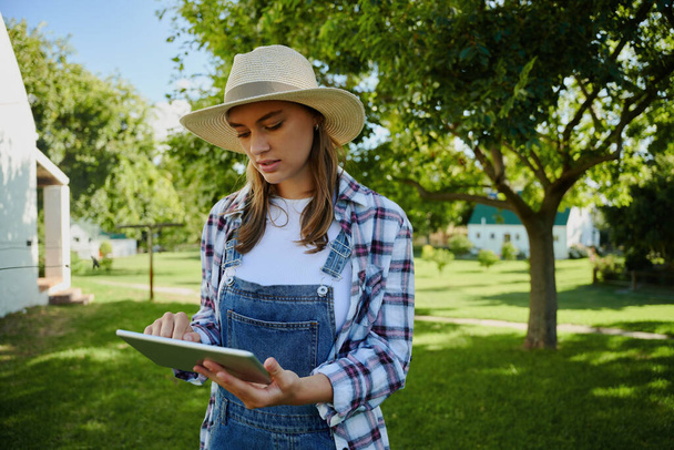Caucasian female farmer standing outdoors typing on digital tablet researching for assignment . High quality photo - Φωτογραφία, εικόνα