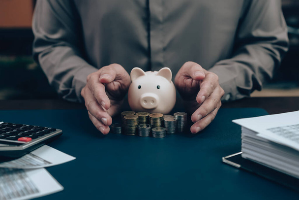 Investors hand protect and save money piggy bank on the table. Business saving money and financial concept. - Foto, afbeelding