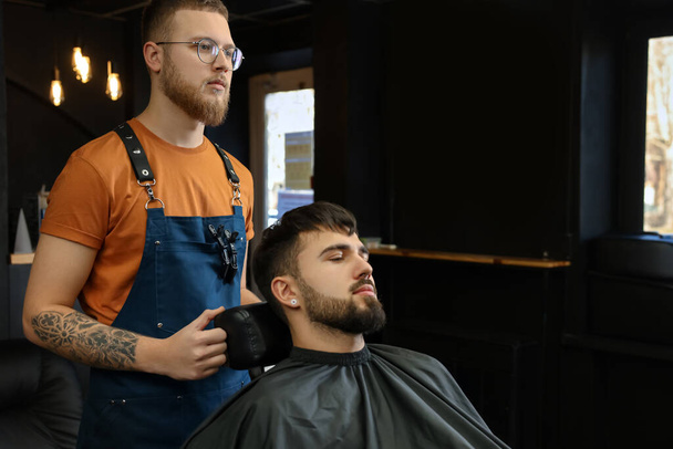 Professional hairdresser working with bearded client in barbershop - Фото, изображение