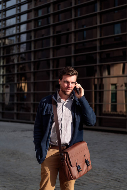 young businessman walking by the offices in the financial district talking on the telephone, concept of entrepreneurship and business, copy space for text - Фото, зображення