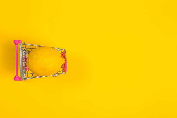 Yellow lemon in a shopping cart on a yellow background, shopping trolley - Fotoğraf, Görsel