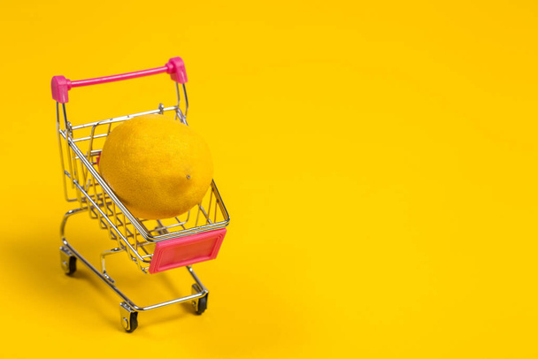 Κίτρινο λεμόνι σε ένα καλάθι αγορών σε κίτρινο φόντο, τρόλεϊ ψώνια - Φωτογραφία, εικόνα