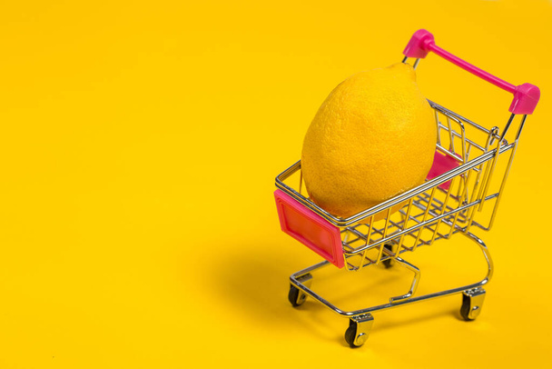 Yellow lemon in a shopping cart on a yellow background, shopping trolley - Φωτογραφία, εικόνα