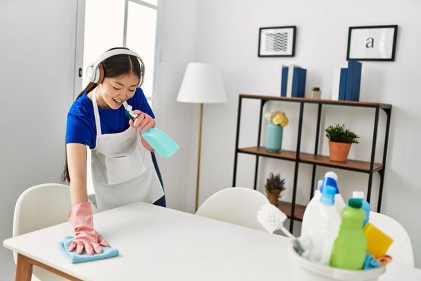 Νεαρή κινέζα νοικοκυρά καθαρισμού και το τραγούδι χρησιμοποιώντας ψεκαστήρα στο σπίτι. - Φωτογραφία, εικόνα