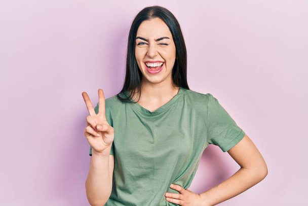 Beautiful woman with blue eyes wearing casual t shirt smiling with happy face winking at the camera doing victory sign. number two.  - Fotografie, Obrázek