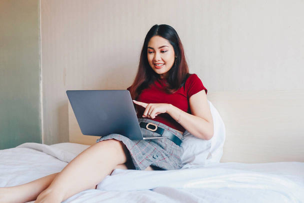Young Asian businesswoman smiling while working on laptop computer at home. Portrait of positive business woman looking at laptop screen indoors - Photo, image