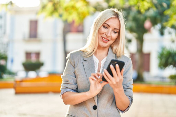 Young blonde woman smiling confident using smartphone at park - 写真・画像
