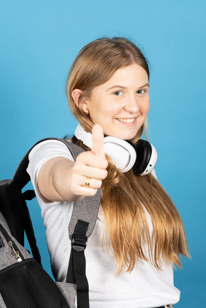 Hübsches Teenager-Mädchen macht ok Zeichen in die Kamera isoliert auf blauem Hintergrund. Porträt eines fröhlichen Gymnasiasten. - Foto, Bild