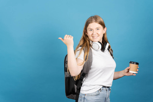 Üniversite öğrencisi mavi arka planda izole edilmiş kopya alanını işaret ediyor. Sırt çantası takan genç kızın portresi.. - Fotoğraf, Görsel