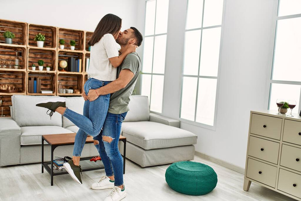 Νεαρό ζευγάρι Λατίνων φιλιούνται και αγκαλιάζονται στο σπίτι. - Φωτογραφία, εικόνα