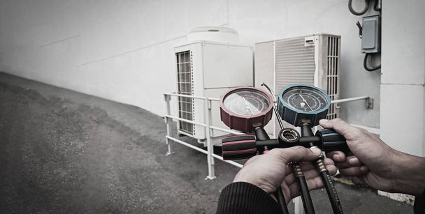 Ilmankorjausmekaanikko, joka käyttää mittauslaitteita teollisuustehtaan ilmastointilaitteiden täyttämiseen ja ulkoilman kompressoriyksikön huollon tarkistamiseen. - Valokuva, kuva