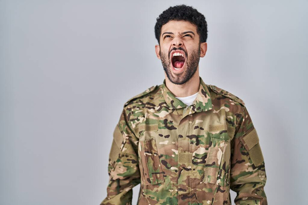 カモフラージュ軍の制服を着たアラブ人の男は怒りと怒りで叫んで、イライラし、激怒叫んで怒っている。怒りと攻撃的な考え方.  - 写真・画像