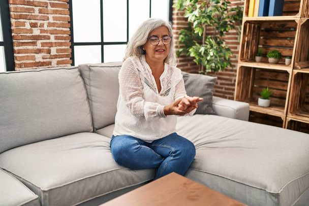 Frau mittleren Alters sitzt auf Sofa und leidet zu Hause unter Schmerzen am Handgelenk - Foto, Bild