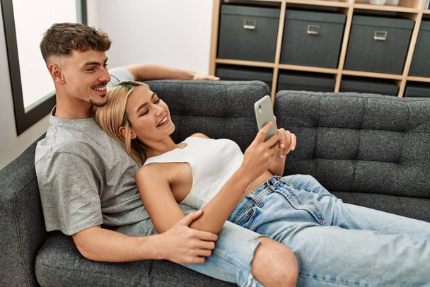 Junges kaukasisches Paar lächelt glücklich mit Smartphone zu Hause. - Foto, Bild
