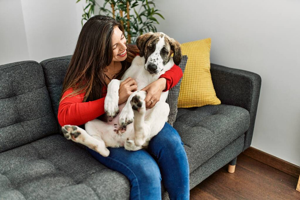 Mujer joven abrazando perro sentado en el sofá en casa - Foto, imagen