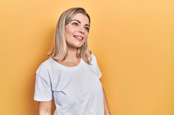 Beautiful caucasian woman wearing casual white t shirt looking away to side with smile on face, natural expression. laughing confident.  - Foto, Bild